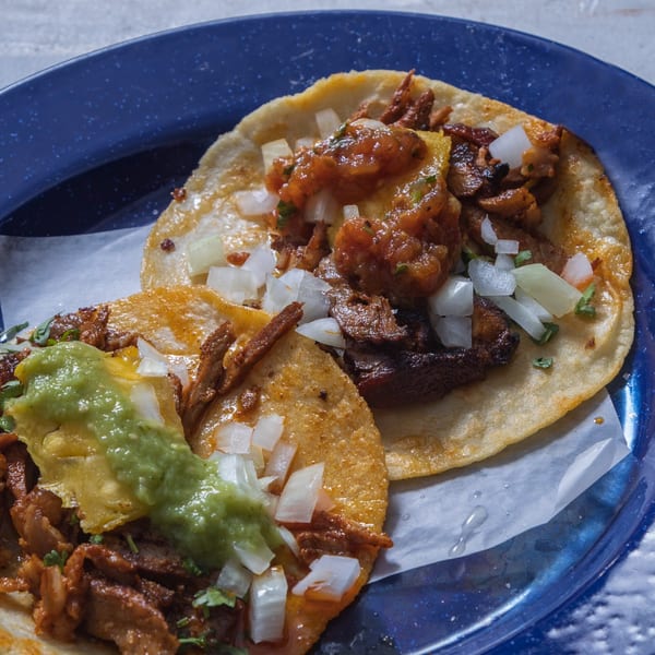 Two delicious tacos with meat, onions, and salsa on a blue plate with white paper.