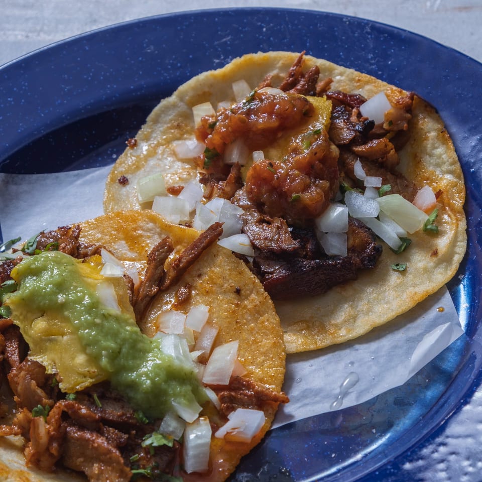 Two delicious tacos with meat, onions, and salsa on a blue plate with white paper.