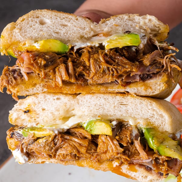 A Picos Restaurant Mexican torta, cut in half, revealing shredded meat, avocado, and crema.