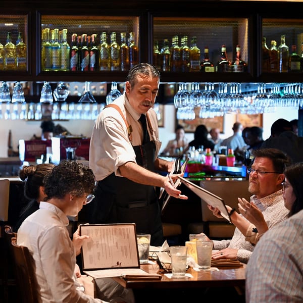 A Picos Restaurant waiter takes orders from a table of four diners in a dimly lit dining room.