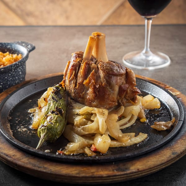 Picos Restaurant's braised pork shank with roasted onions and a charred green pepper on a sizzling platter.