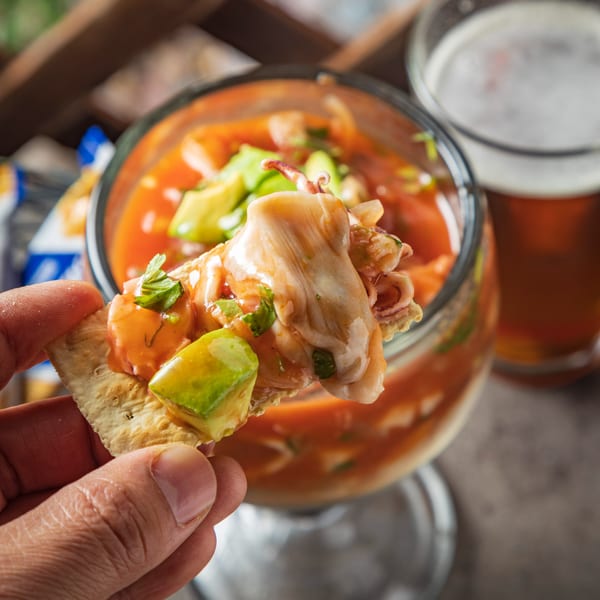 Hand holding a cracker topped with Picos' Mexican seafood cocktail, avocado, and cilantro.