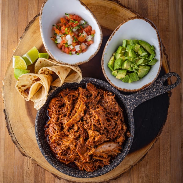 Picos Restaurant's Mexican dish with shredded meat, tortillas, pico de gallo, and avocado on a wooden board.