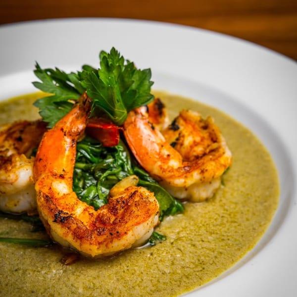 Spiced shrimp and sautéed greens on a bed of green sauce, garnished with parsley.